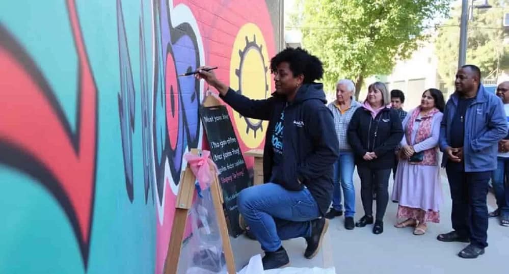 An artist busy working on a mural as other people look on—should an artist work for free?