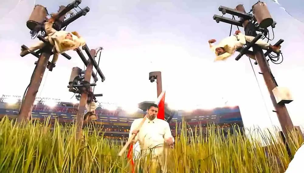 Bad Bunny Super Bowl halftime show performance art featuring the artist walking through a grassy installation while dancers on power lines simulate repairs.