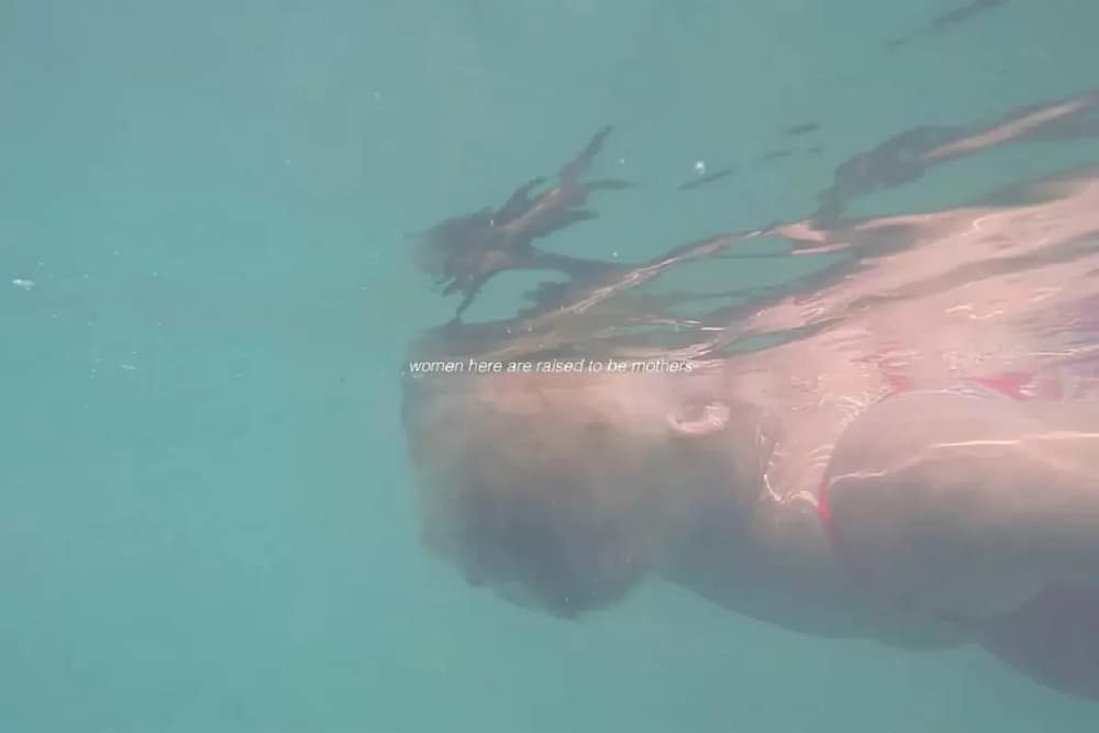 Film still titled Retiro by Natalia Lassalle-Morillo showing a woman swimming on her back with text overlay reading Women here are raised to be mothers, exploring hydro-politics and borders.
