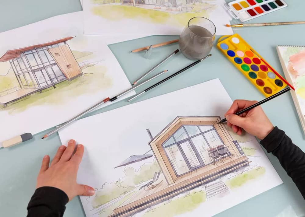 An architect illustrator working on a hand drawn illustration of a modular house using black pencil to draw lines on a sketch. Common Misconceptions has given prefab homes a bad name