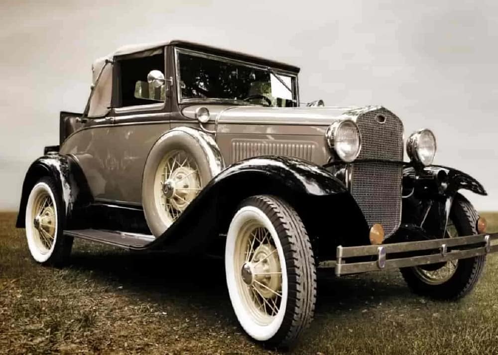 A old, classic car with a shiny bronze coat is parked in the middle of a field with an overcast of clouds overhead. Learn about the art and design behind classic cars like this.