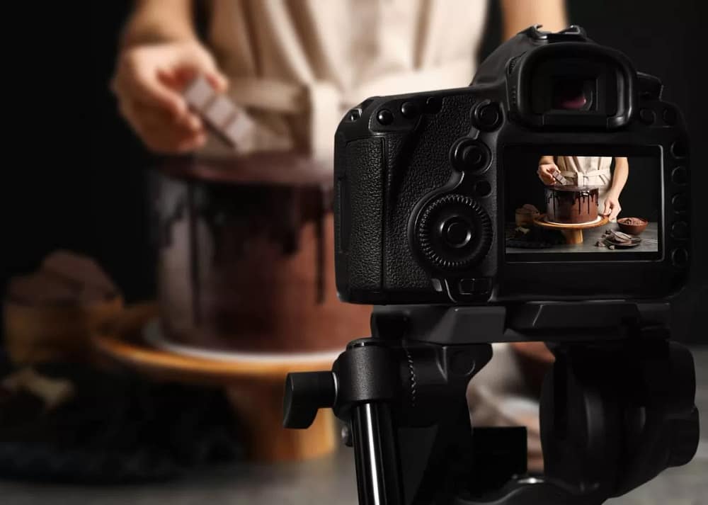 A studio area with a chef preparing to photograph a chocolate cake with a black curtain background. Capturing the beauty of desserts requires knowing how to effectively capture these sweet masterpieces