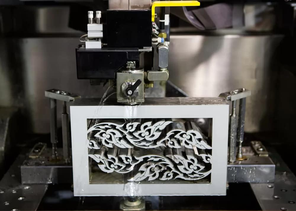An electrical discharge machine cuts a metal art piece in the shape of a box with intricate designs in the middle. Art fabrication process from concept to creation requires diligence and creativity .