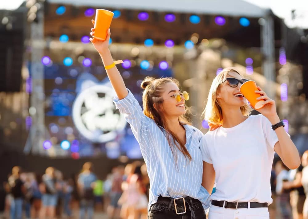 Two women stand together at a music festival. They're both drinking out of orange cups, and one girl raises the cup in the air. If you intend to have as much fun as these people, follow our top tips to prepare for a musical festival in Chicago