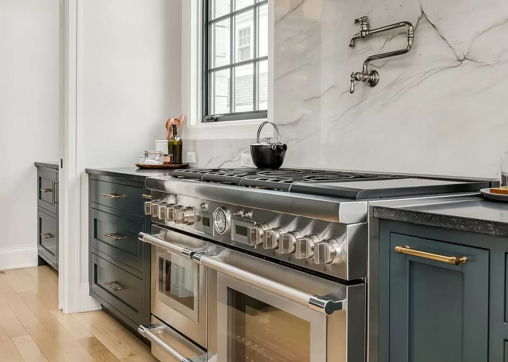 A luxury kitchen with green cabinets, wood floors, black countertops, a stainless steel double oven, and a gas stove top. Examples of Must-Have Features for a Chef-Worthy Kitchen