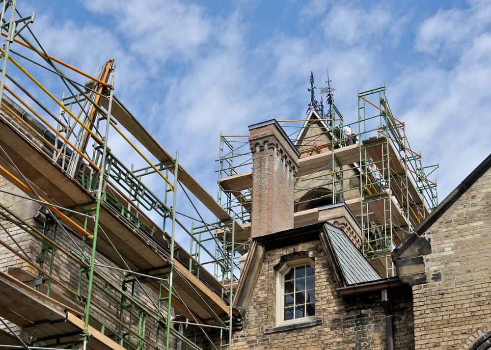 Metal scaffolding against the surface of a large building comprised of old brick, with blue skies in the background. These tips for architects with big dreams in building restoration are for aspiring architects