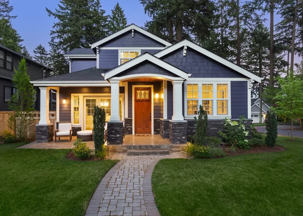 The exterior of a home with blue siding and immaculate landscaping. The front porch lights are on with the sky darkening. The beautiful color combination is the secret to creating a cohesive exterior design