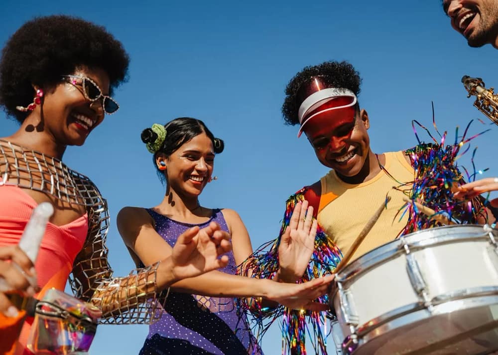 A group of culturally diverse friends celebrate carnival with drums and other instruments while dancing. Drumming and dancing are two reasons why designing public spaces for multicultural celebrations is essential.