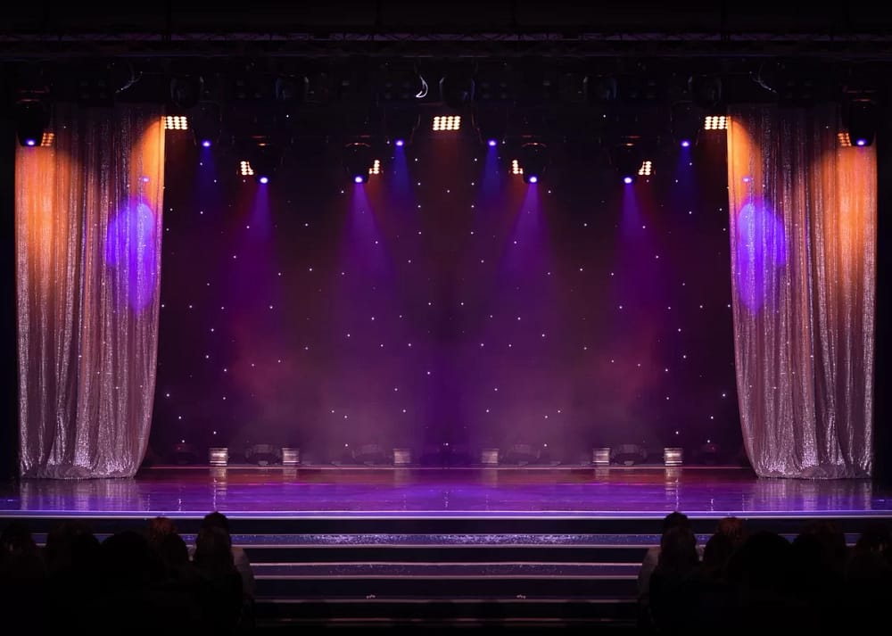 A dramatic stage contains purple and orange lights, shimmering silver curtains, and a dark, starry backdrop. It demonstrates how technology and AI is impacting the evolution of theater.