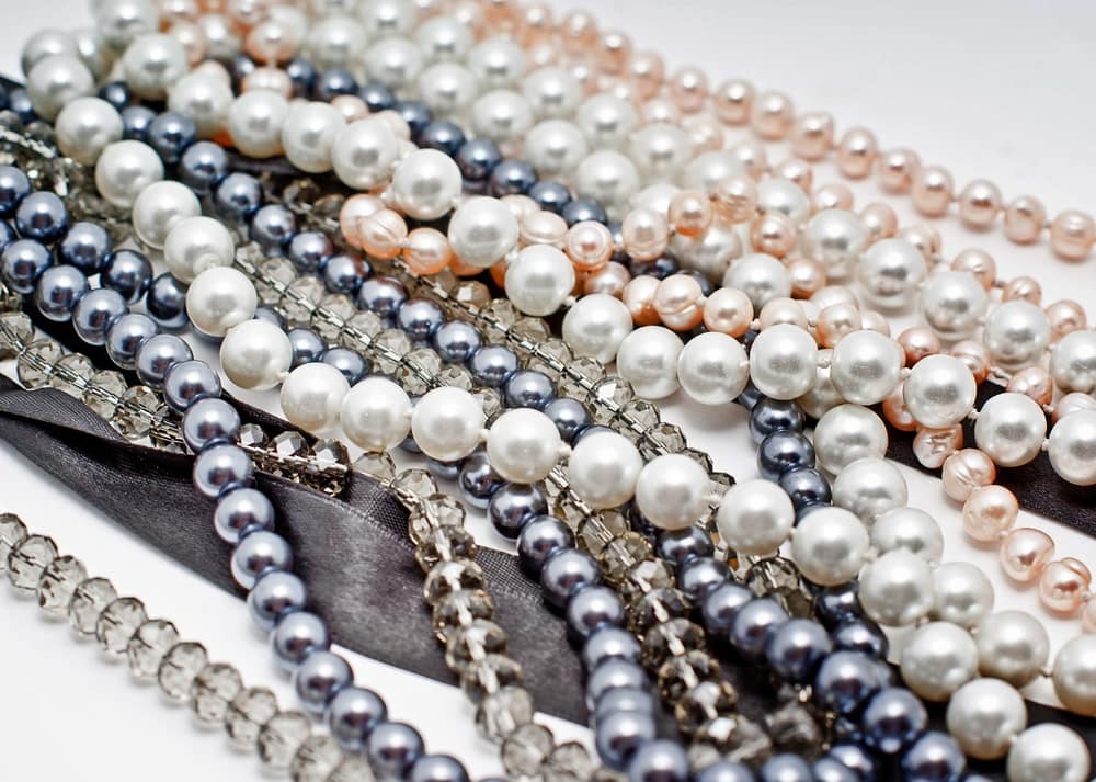 A group of pearl necklace strands with different pearl sizes and colors arranged in loose overlapping loops.