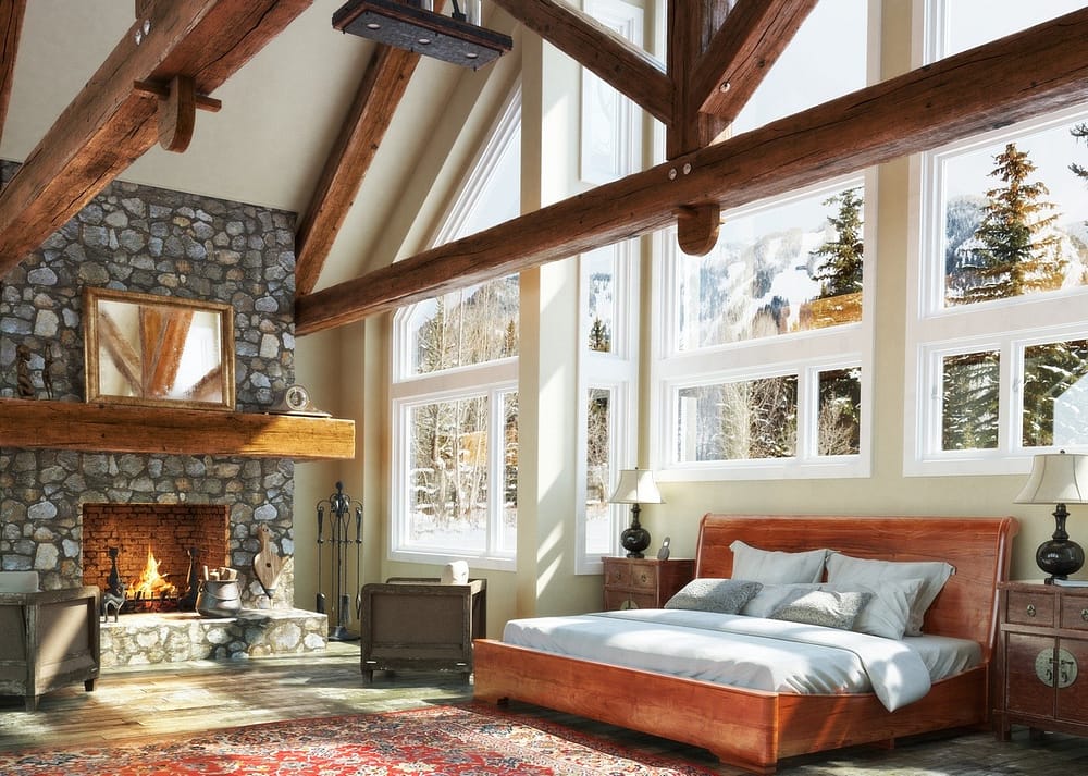 Open concept cabin bedroom with a fireplace, bed, sofa, and large windows showing a snowy outdoor view of the forest.
