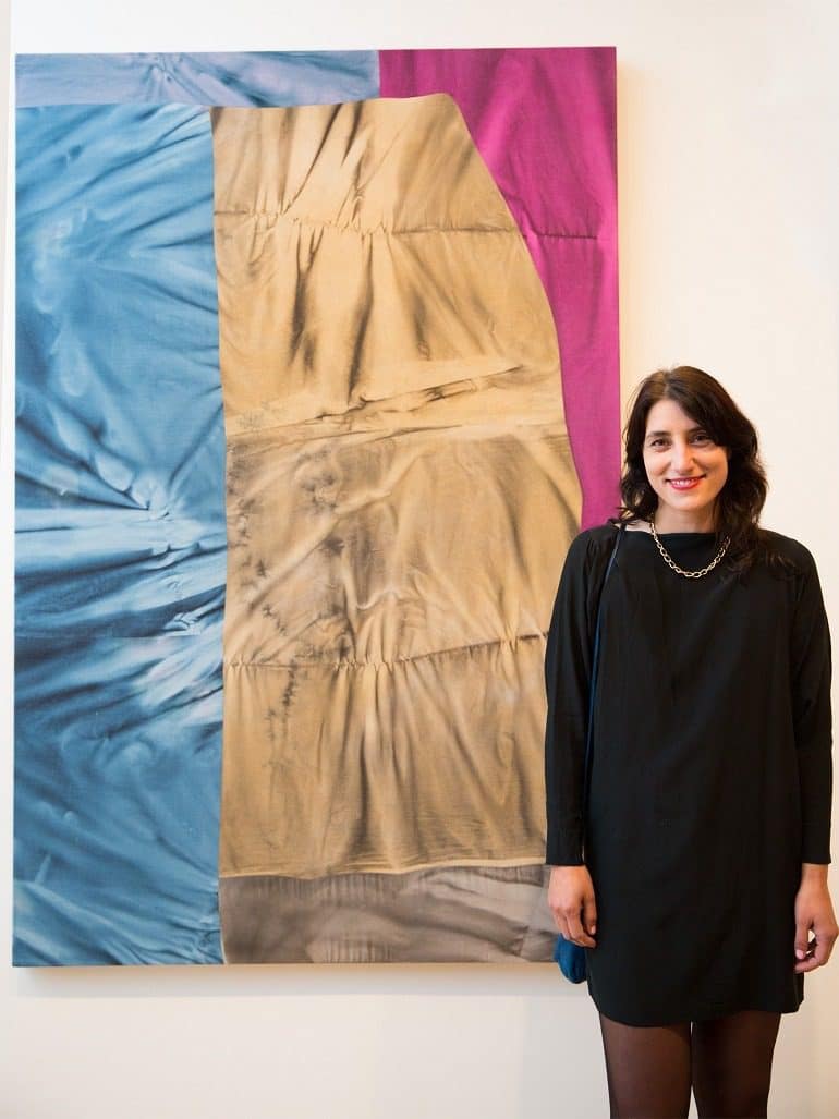 Image -Artist Colleen Heslin stands in front of her painting with brown, blue and red color. She is the winner of the RBC Canadian Painting Competition, with her work entitled Almost young and wild and free.
