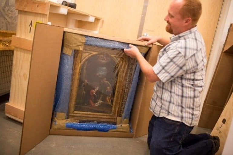 Image- Shows Chris Rupp, Westmont Museum collections manager kneeling as he carefully uncrates the Tisi painting. 