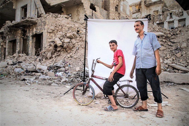 Image: Photograph of boy on a bicycle and a man in front of a white background is one of the photographs by Iranian photographer Amir Kabir Jabbari highlighting the lives of children in Syria