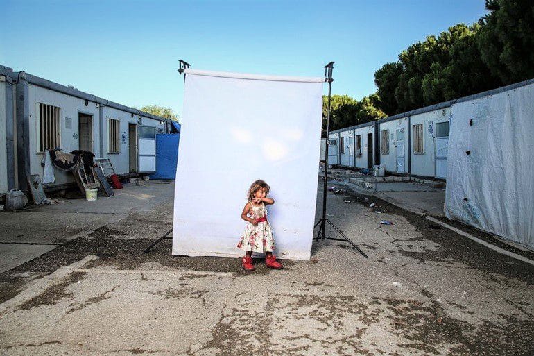 Image: Photograph of a girl wearing sleeveless dress with flower motifs and red shoes in front of a white background is one of the photographs by Iranian photographer Amir Kabir Jabbari highlighting the lives of Syrian Civil War children
