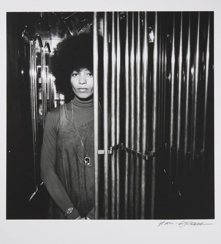 Image- Shows Angela Davies behind some bead curtins. It was taken by Portrait Photographer Hans Gedda, one of Sweden’s leading portrait photographers